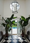 Diele mit schwarzweissem Schachbrettboden und Pflanztöpfen mit Bananenpflanzen; Blick auf Pool durch geöffnete Fenstertür