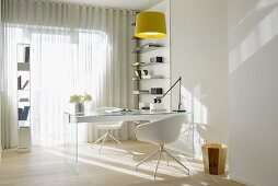 Glass desk, white designer chairs and airy storage shelves in office flooded with sunlight