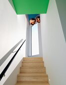 Pale wooden staircase with black handrail in narrow stairwell with copper-coloured pendant lamps over landing and green-painted ceiling