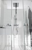 A glazed shower cubicle with a double swing door, a rain shower head and the hand-held shower head on a white tiled wall