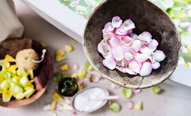 A bowl of rose petals on the edge of a bathtub filled with a scented petal bath