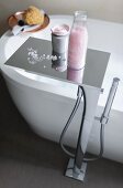 A chrome-plated floor tap with a waterfall spout and a shelf of bathing utensils