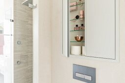 A small cupboard built into a wall niche with an open door and a view of bathroom utensils