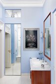 Waschtisch mit Unterschrank aus mahagonyfarbenem Holz und gerahmter Spiegel vor hellblau getönter Wand, im Hintergrund Einbauschrank mit Spiegeltüren