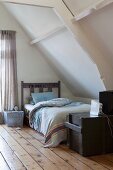 Bett aus Holz in Jugendzimmer unterm Dach; alte, schwarz lackierte Transportkiste am Fussende