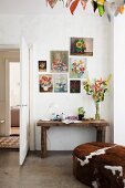 Collection of classic, floral, still-life paintings above rustic console table and pouffe with animal-skin cover below garland of fabric love-hearts