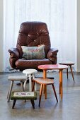 Retro collection of various stools and side tables in front of cushion with 'Happy' motif on leather swivel chair
