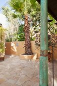 Wooden column with distressed green paint on Mediterranean terrace with palm trees