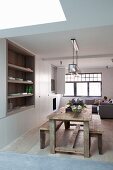 Rustikaler Esstisch und Bänke vor integriertem Wandregal im offenen, schlichten Wohnraum