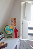 Globe lamp and red garden gnome ornament on built-in desk next to window with interior, folding shutters