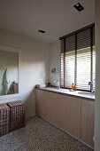 Ample storage in fitted washstand below window with half-opened louvre blind