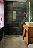 Modern bathroom, glass partition screening shower area with black wall tiles and solid-wood washstand