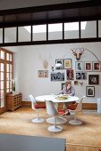 Woman sitting on Tulip chair at matching table in front of framed photos on white wall