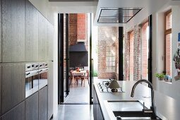 Contemporary kitchen with counter opposite fitted cupboards; view of dining room with exposed brick wall through open door