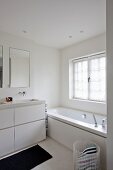 Washstand with white base unit next to bathtub below window in contemporary bathroom