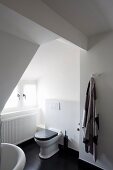 Toilet in white, attic bathroom with black wooden floor