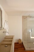 Naturtöne im Bad: Waschtisch mit Kaskadenbecken und Duschkabine aus Beton, daneben Holzklotz als Ablage