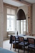 Dining area in purist, renovated period building; pendant lamp with rough lampshade, wooden armchairs with cane backrests and seat cushions