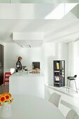 Open-plan, white designer kitchen with dining area and kitchen counter; woman in background
