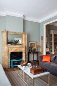 Delicate coffee table and open fireplace in elegant living room with grey-painted walls and stucco moulding