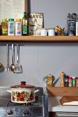 Retro saucepan on gas cooker below spices on narrow shelf