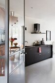 Blick durch offene Tür in Küche mit schwarzen Unterschränken und Betonboden