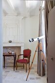 Telescope at window with floor-length curtains, antique chair and Rococo-style side table in front of fireplace