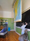 Child's bedroom with retractable map of world and boy and dog standing in front of long blackboard on wall