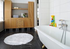 Colourful bathtub toy on free-standing bathtub with retro tap fittings; cabinets with integrated shelves in background