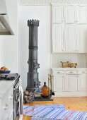 Antique iron stove in white, country-house kitchen with woven rug on plain wooden floor