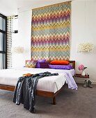 Expressive, colourful zig-zag wall hanging above double bed with brightly coloured pillows and designer pendant lamps