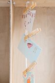 Cards with colourful motifs hung from vertical cord using clothes pegs