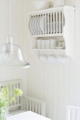 Plate rack with cup hooks and pendant lamp with glass lampshade above dining set in white, Scandinavian kitchen