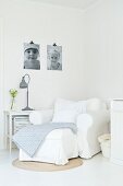 White armchair in corner, grey lamp on side table and black and white photos on wall