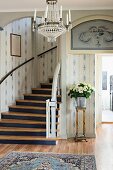 Foyer with white and blue wallpaper, curved staircase and bouquet in silver vase on plant stand
