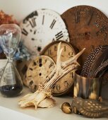 Antlers, brass pot of feathers and vintage clock faces on white shelf
