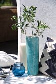 Olivenzweige in türkisfarbener Bodenvase, Windlicht aus Glas, Bodenkerze und Kissen