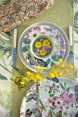 Floral crockery, table runner and sprig of yellow flowers viewed from above