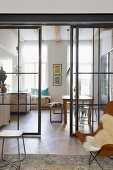Blick vom Wohnraum mit Klassikersessel durch verglaste Stahlschiebetüren in die offene Küche mit Essplatz