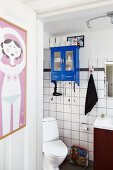 Blick durch offene Tür mit aufgehängtem Poster auf Toilette und blau lackiertes Hängeschränkchen