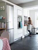 Woman in contemporary kitchen with white, fitted cupboards and integrated fridge