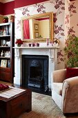 Wall decorated with dark red section above picture rail and floral wallpaper below in traditional interior; antique mirror above English fireplace
