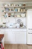 Simple, white kitchen counter with vintage crockery on wall-mounted shelves and retro-style fridge