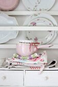 Pink saucepan and floral tea towels in front of vintage plates on plate rack