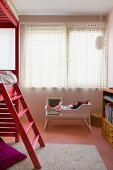 Dolls' cradle painted white below window with closed curtains and wooden loft bed with ladder stained light red
