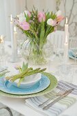 Pastel place setting with asparagus spears and glass vase of tulips on festively set table