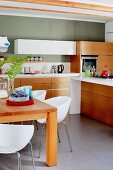White shell chairs around wooden table in kitchen with modern counters, solid wooden fronts on base units and grey-painted walls