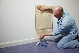 Mann beim Anpassen von Lincrusta (Strukturtapete aus linoleumähnlichem Material) an Wand