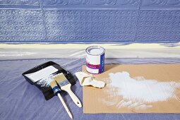 Malerutensilien auf Boden vor Lincrusta (Strukturtapete aus linoleumähnlichem Material) an Wand, blau bemalt