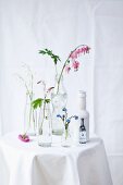 Forget-me-nots, lily of the valley, foamflowers and bleeding heart in bottles on table with white tablecloth